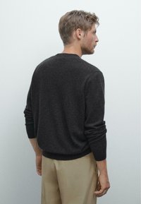Donkergrijze trui met lange mouwen, geribbelde manchetten en zoom. Zachte textuur, klassiek ontwerp met ronde hals. Gestyled met beige broek.