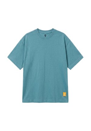 Niebieski t-shirt z krótkim rękawem i okrągłym dekoltem z małą żółtą kwadratową naszywką blisko dolnego brzegu na białym tle.
