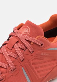 Zapatilla deportiva roja con parte superior sintética texturizada, cordones con patrón y etiqueta Gore-Tex, con un interior acolchado y suela de goma.