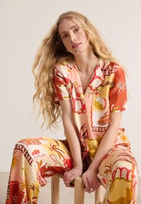 Conjunto de pijama de mangas cortas, con un estampado floral y geométrico en rojo, rosa y amarillo sobre un fondo crema, hecho de una tela suave.