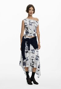 Weißes asymmetrisches Outfit mit abstraktem schwarzen und blauen Zeitungsdruck. Das Oberteil hat ein Schulterfreies Design; der Rock verfügt über einen dunkleren gestrickten Taillengürtel.