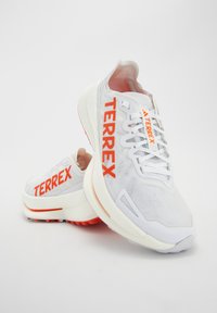 Paire de baskets blanches avec lettrage orange "TERREX", tige en mesh et semelles épaisses et rembourrées sur fond blanc uni.