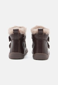 Bruna läderankelboots med fluffig beige foder, utrustade med två justerbara Velcro-remmar och en texturerad gummisula.