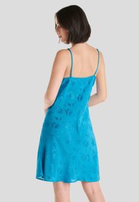 Un vestido de satén azul con tirantes finos, que presenta un patrón floral y un ligero brillo. El diseño es hasta la rodilla y tiene un corte holgado.