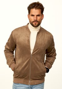 Braune Wildleder-Bomberjacke mit Frontreißverschluss, gerippten Bündchen und Saum sowie seitlichen Taschen, getragen über einem cremefarbenen Rollkragenpullover.