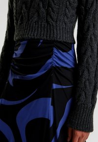 Gestrickter, anthrazitfarbener Pullover mit Kabelmuster, kombiniert mit einem schwarzen Rock, der auffällige blaue Wirbel und geraffte Details an der Taille aufweist.