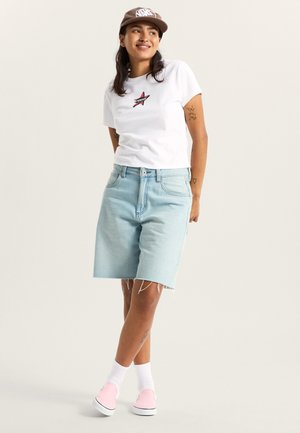 Jasnoniebieskie szorty dżinsowe z postrzępionym dołem, zestawione z białą koszulką z czerwonym logo w kształcie gwiazdy i różowymi butami slip-on w białych skarpetkach.