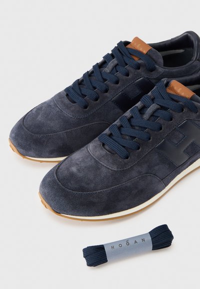 Ναυτικά σουέτ αθλητικά παπούτσια με ομαλή υφή, ανοιχτό καφέ λεπτομέρειες και στρογγυλά κορδόνια. Περιλαμβάνει επιπλέον ζευγάρι ναυτικών κορδονιών. Λαστιχένια σόλα.