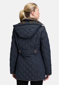 Marineblå quiltet jakke med hætte, der har en indsnævret talje, brune detaljer og et mønstret indvendigt foer. Tekstureret stof med diamantmønster.
