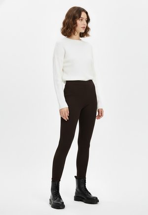 Black ribbed leggings paired with a white knit sweater, featuring long sleeves and a round neckline, complemented by black lace-up boots.