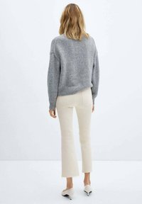 Suéter corto de color gris claro en punto suave con bajo acanalado, combinado con jeans cremosos de campana con bajo deshilachado y zapatos de tacón en tono neutro.