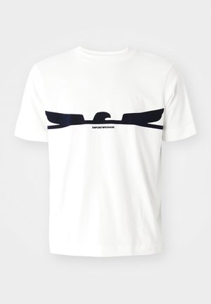 T-shirt blanc à manches courtes avec un large motif noir d'aigle sur la poitrine et le texte « Emporio Armani » sous la tête de l'aigle.