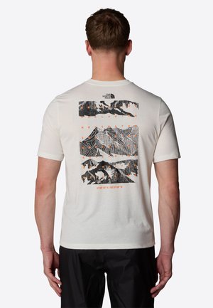 Homme portant un t-shirt blanc avec des graphiques de montagne en noir et orange et des lignes de contour, ainsi que le logo The North Face dans le dos.