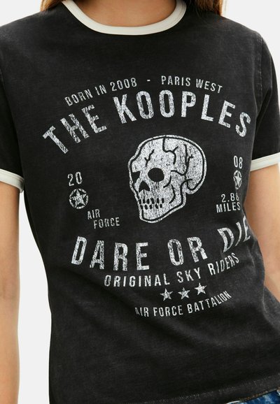 Juodas marškinėliai su vintage kaukolės grafika, balta tekstu, raglan rankovėmis su grietinėlės spalvos apdaila ir nusidėvėjusiu tekstūru. Dėvi šūkį "Drąskis arba mirti".