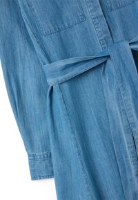Abito in denim blu con due tasche sul petto, maniche lunghe e una cintura coordinata in vita. Tessuto morbido con una leggera sfumatura.