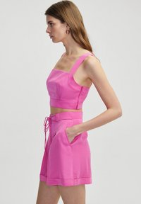 Fitted pink crop top with square neckline and wide straps, paired with high-waisted shorts featuring tie detail and side pockets.