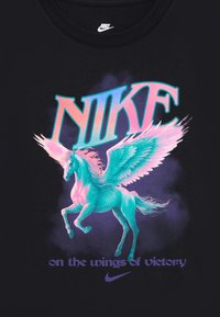 Juodas medvilninis marškinėliai su grafiką vaizduojančia sparnuotą vienaragį mėtine ir rožine spalvomis, su „NIKE“ ir fraze „ant pergalės sparnų.“