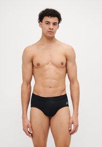 Mustat urheilutrikoot, jotka on valmistettu sileästä kankaasta ja joissa on tiukka muotoilu. Vyötäröllä on logo, ja lahkeissa on klassinen leikkaus.