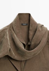 Oliven Grøn, blød ruskindsjakke med en draperet krave og strukturerede skuldre. Har et mærke med "Massimo Dutti" indeni. Glat tekstur.