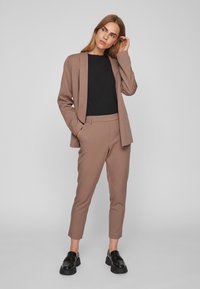 Pruun kohandatud bleiser ja sobivad püksid, must tihe topp ja mustad loafer-kingad. Sile kangas, sirge lõige, peene tasku detail.