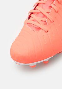 Crampon de football rose vif avec tige synthétique texturée, fermeture à lacets et semelle extérieure blanche dotée de quatre crampons orange pour l'adhérence.