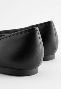 Schwarze Lederballerinas mit einer glatten Textur, gebogenem Rückendesign und verstärkten Nähten entlang der Kanten. Minimalistische Bauweise, keine Verzierungen.