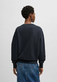 Black sweatshirt with drop shoulders, ribbed cuff details, and a round neckline; paired with a denim skirt showcasing stitching and pockets.
