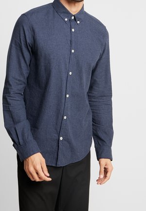 Marineblaues Hemd mit Knopfleiste aus strukturiertem Stoff, mit langen Ärmeln und spitzem Kragen, versehen mit kontrastierenden weißen Knöpfen.