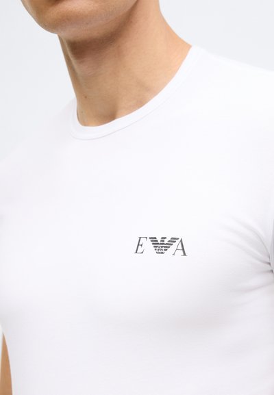 Balta īsroku T-krekls no gludas kokvilnas ar apaļu kakla izgriezumu. Uz krūtīm redzams neliels tumši pelēks logotips.