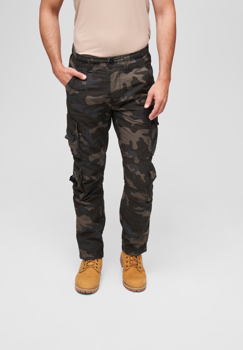 Camo cargo pants in dark green and black, featuring multiple pockets, a relaxed fit, and a sturdy fabric. Paired with tan boots.