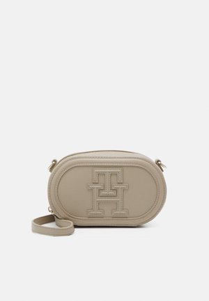 Beige oval crossbody bag with embossed interlocking "TH" logo, zipper closure, and detachable wrist strap on a plain background.