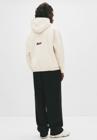 Kremowa bluza z kapturem, z bordowym logo na plecach. W połączeniu z czarnymi, luźnymi spodniami i beżowymi sneakersami.