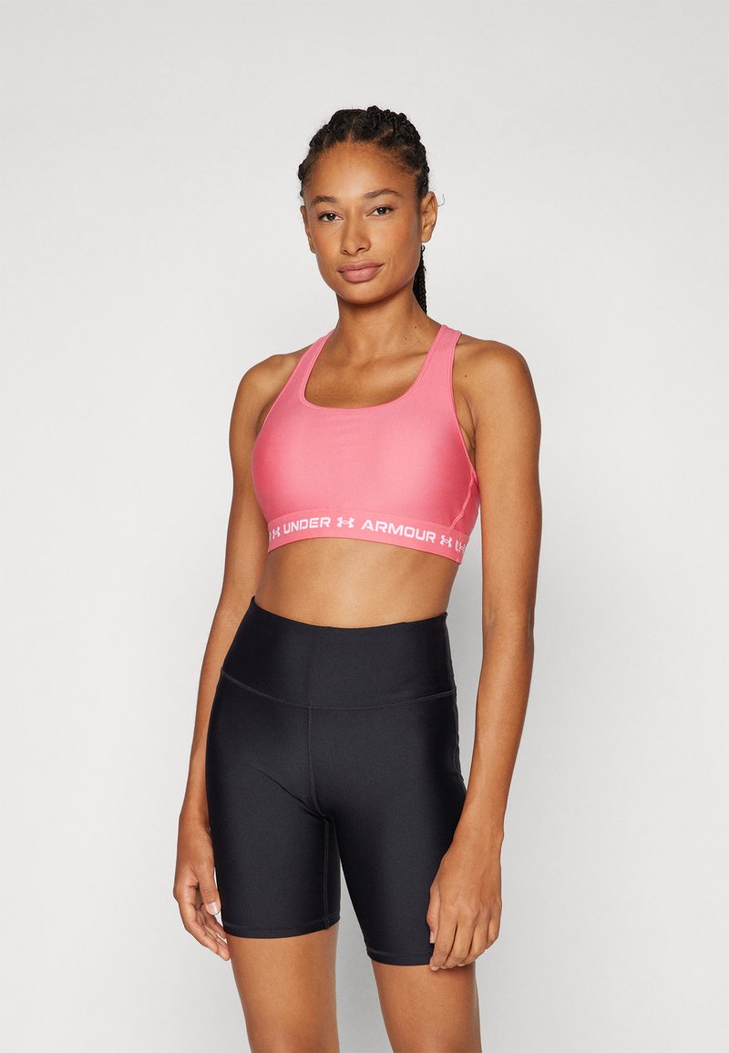 Sutien sport roz cu bretele late și logo-ul Under Armour; asortat cu pantaloni scurți negri cu talie înaltă; ambele realizate dintr-un material neted și elastic.