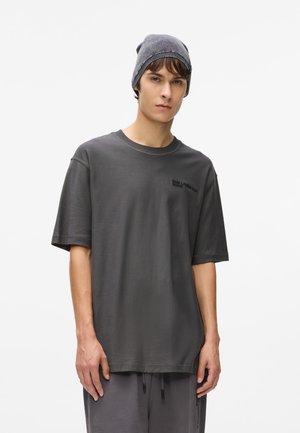 Grå oversized t-shirt med korta ärmar, ribbat rundhalsat halslinning och subtilt logotyp på bröstet. Buren med en matchande mörkgrå beanie.