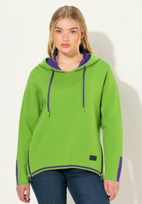 Felpa verde con cappuccio e dettagli viola, dotata di una cerniera laterale, tessuto testurizzato e un design dalla vestibilità ampia.