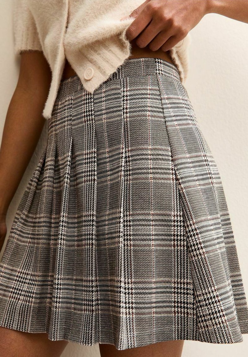 Szara plisowana spódnica w kratę wykonana z tkaniny o wzorze pepitki i kratki, z subtelnymi czerwonymi akcentami, długości do połowy uda.