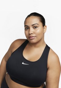 Svart sports-BH laget av glatt stoff, med scoop-halser og brede stropper. Nike-logo i hvitt plassert midt på brystet.