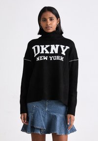 Svart stickad tröja med hög krage, med vit "DKNY NEW YORK" logotyp. Kombinerad med en jeanskjol med fläktande volangdesign.