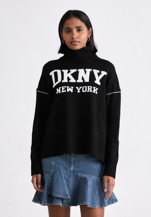 Schwarzer gestrickter Pullover mit hohem Kragen, der das weiße Logo "DKNY NEW YORK" zeigt. Kombiniert mit einem Jeansrock im ausgestellten Rüschendesign.