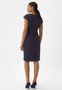 Körperbetontes navyfarbenes Kleid mit Capärmeln, Rückenventilation und verdecktem Reißverschluss. Kombiniert mit passenden spitzen Absätzen und schlichten Ohrringen.