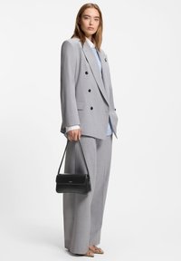 Lysegrå dobbeltradet blazer kombineret med løse grå bukser. En blåstribet skjorte under og en sort håndtaske medfølger.
