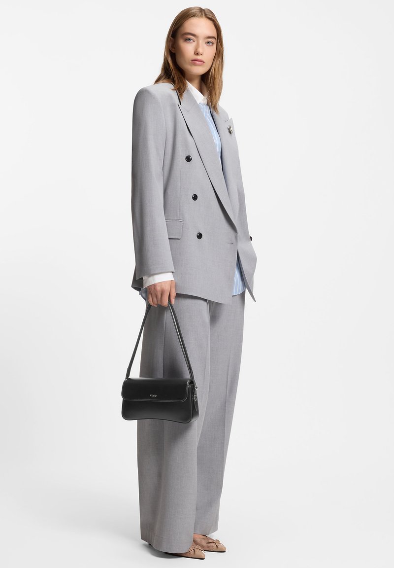 Lysegrå dobbeltradet blazer kombineret med løse grå bukser. En blåstribet skjorte under og en sort håndtaske medfølger.