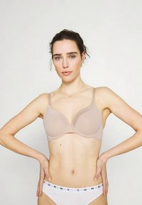 Beige padded bra with adjustable straps and smooth fabric, featuring a subtle sheen and rounded cups for standard support.