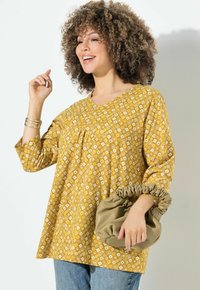 Haut à motifs jaunes avec un col en V et des manches trois-quarts ; associé à un sac à main en beige doux et froncé. Coupe décontractée avec un tissu texturé.