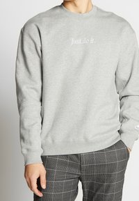 Šedá mikina s kulatým výstřihem, žebrovými manžetami a spodním lemem, na hrudi s textem "Just do it." Spárováno s kalhotami s kostkovaným vzorem.