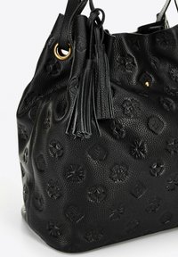 Sac à main en cuir noir texturé avec des motifs embossés, œillet doré, et deux pompons en cuir suspendus à la bandoulière.
