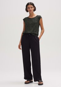 Schwarze Bluse mit floralem Muster und kurzen Ärmeln, kombiniert mit lockeren schwarzen Hosen und einfachen schwarzen Sandalen. Weicher Stoff mit lässigem Schnitt.