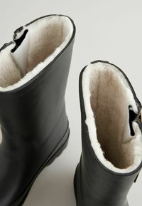 Schwarze Gummistiefel mit einem weichen, weißen Kunstfellfutter oben, einem glatten äußeren Design und einer abgerundeten Öffnung.