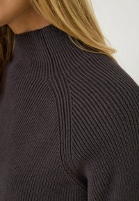 Pull en maille côtelée gris foncé avec un col haut et des détails texturés le long des épaules, fabriqué dans un matériau en tricot doux.
