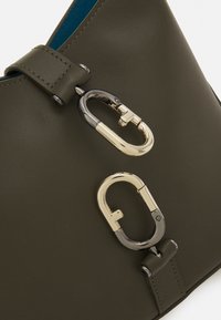 Oliivivihreä nahkalaukku, jossa on kultaisia ja mustia metalliosia sekä soljellinen yksityiskohta. Sisäpuolella on kontrastivärinen sininen vuori.